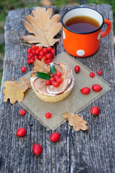 Romantic autumn still life with basket cake, cup of tea, rowan berries and leaves at wooden board