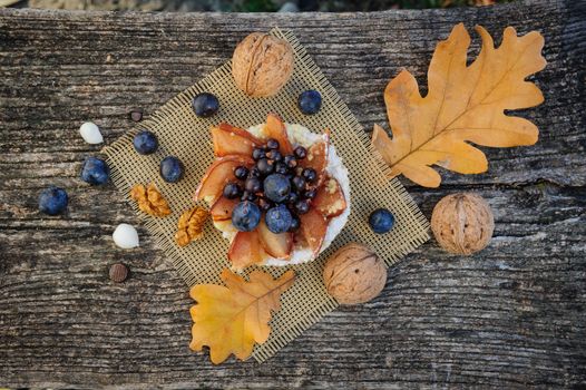 Romantic autumn still life with blackthorn berries in blue bowl and bagel on wooden board