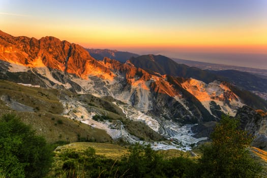 Panoramic sunset views of the marble quarries of Carrara with shoreline in the background