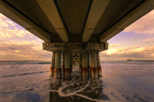 View of seascape from under a piermarine pillars lit by morning sun