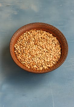 Green lentil in wooden bowl, on blue background