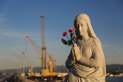 Close up view of the Virgin Mary patroness of seafarers and port with cranes in the background