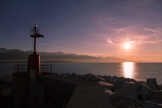 Costal landscape with lighthouse in backlight and the mountain range in the background