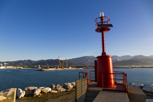 Costal landscape with lighthouse in the foreground, the commercial port and the mountain range in the background