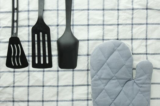 black ladle, kitchen glove and spade of frying pan on the white table