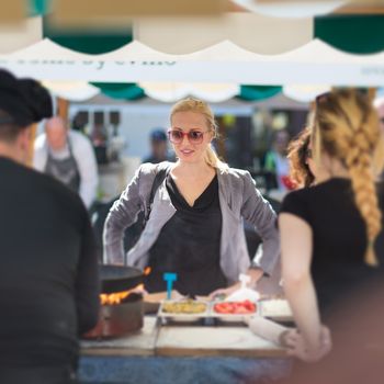Beautiful blonde caucasian lady buying freshly prepared meal at a local street food festival. Urban international kitchen event in Ljubljana, Slovenia, in summertime.