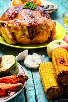 Whole roasted chicken with baked vegetables on wooden background
