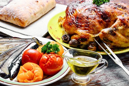 Whole roasted chicken with baked vegetables on wooden background