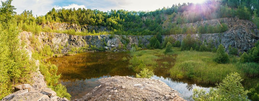 panorama of abandoned and flooded quarry, Czech Republic, teal and orange color tone. Beautiful landscape with sun flare.