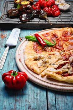 Italian pizza with meat and baked vegetables on the kitchen board