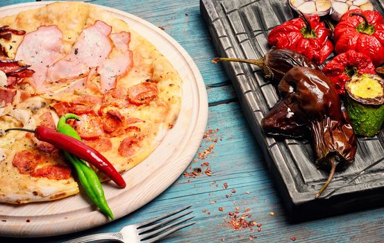 Italian pizza with meat and baked vegetables on the kitchen board