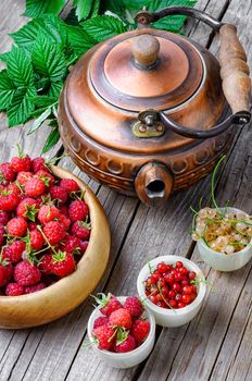 Kettle and summer berries currants and raspberries on wooden background