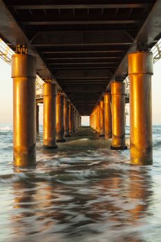 View of seascape from under a piermarine pillars lit by morning sun