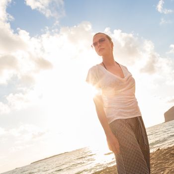 Relaxed woman enjoying sun, freedom and life an a beautiful sandy beach. Young lady feeling free, relaxed and happy. Vacations, freedom, happiness, enjoyment and well being.