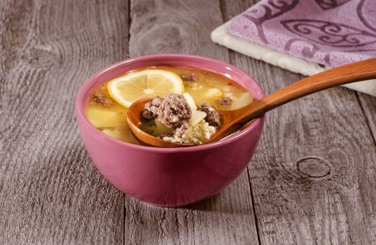 Italian meatball soup and lemon in a bowl, a wooden spoon on old wooden background