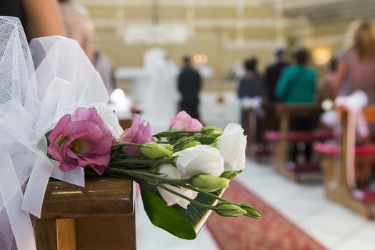 In close up view of flowers that decorate a church and the newlyweds on background