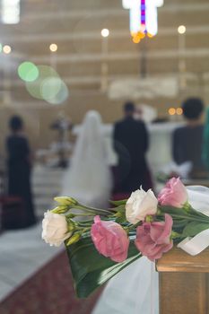 In close up view of flowers that decorate a church and the newlyweds on background