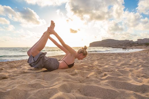 Active young woman streching and practicing yoga on beach at sunset.