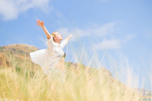 Relaxed woman, arms rised, enjoying sun, freedom and life an a beautiful beach. Young lady feeling free, relaxed and happy. Concept of vacations, freedom, happiness, enjoyment and well being.