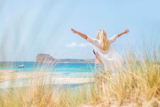Relaxed woman, arms rised, enjoying sun, freedom and life an a beautiful beach. Young lady feeling free, relaxed and happy. Concept of vacations, freedom, happiness, enjoyment and well being.
