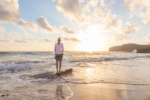 Relaxed woman enjoying sun, freedom and life an beautiful beach in sunset. Young lady feeling free, relaxed and happy. Concept of vacations, freedom, happiness, enjoyment and well being.