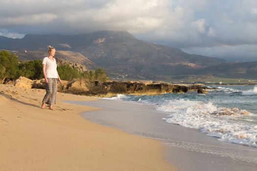Woman walking on sand beach at golden hour. Seashore sunset walk.