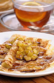 Breakfast pancakes on apples with caramel and chocolate and cup of tea