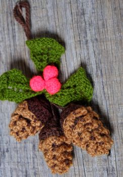 Nice handmade ornament for winter holiday, group of knitted pinecone, holly leaf, berries knit from yarn, message Merry Christmas on tag, nice Xmas background