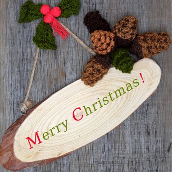 Nice handmade ornament for winter holiday, group of knitted pinecone, holly leaf, berries knit from yarn, message Merry Christmas on tag, nice Xmas background