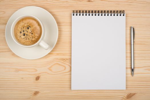 Coffee cup, spiral notebook and pen on the wooden table