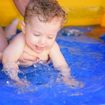 Mom helps her baby to swim in a small paddling pool