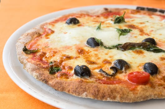 typical italian pizza with mozzarella, tomato cherry and olives  on white plate.