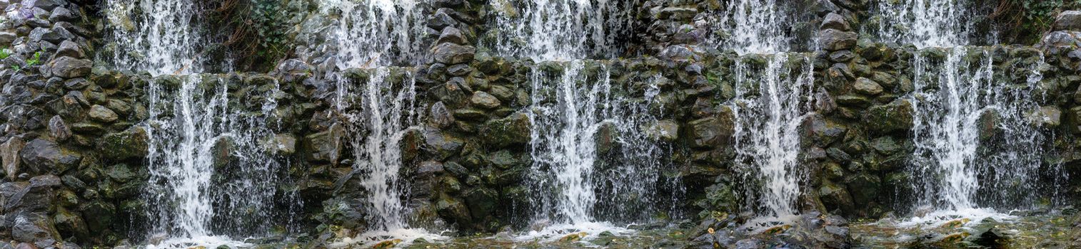 Panorama waterfall, cascade flowing over mossy boulders in a botanical garden.