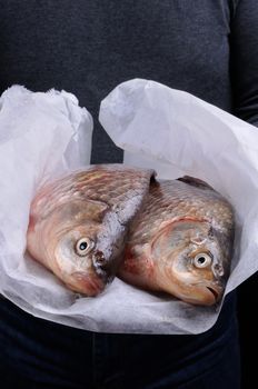 Man holding fresh crucian carp stacked on paper