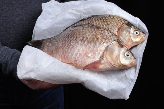 Man holding fresh crucian carp stacked on paper