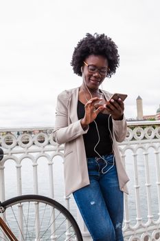 Beautiful African woman chatting with your mobile near a fence promenade in the city