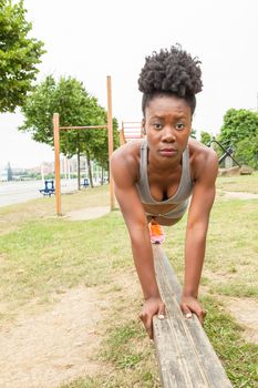 African young woman doing push-ups exercises in urban structures for sports in a city park