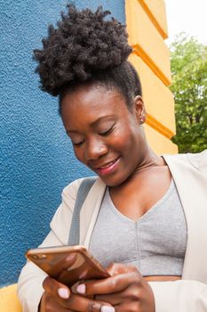 Medium shot of an african young woman in sportswear looking at his mobile phone with a colorful wall blue and yellow