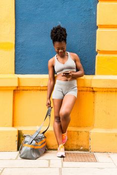 Modern African woman athlete resting on a colorful blue wall with her sports bag