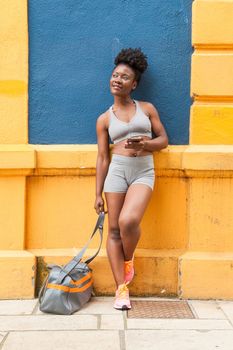 Modern African woman athlete resting on a colorful blue wall with her sports bag