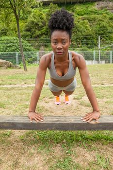 African young woman doing push-ups exercises in urban structures for sports in a city park