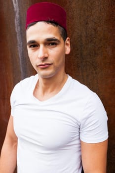 Portrait of a young man with a fez cap next to a oxide wall