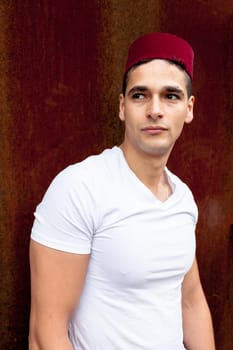 Portrait of a young man with a fez cap next to a oxide wall