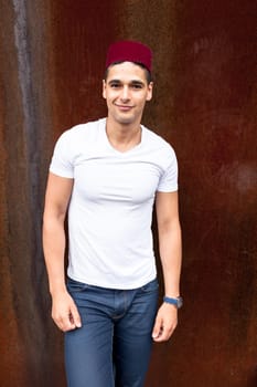 Portrait of a young man with a fez cap next to a oxide wall