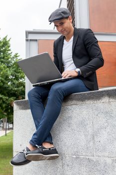 Young man with Irish beret sitting on a wall with a laptop