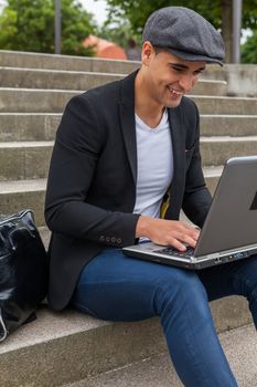 Young man with Irish beret sitting on a wall next to an urban stairs and a shoulder bag near