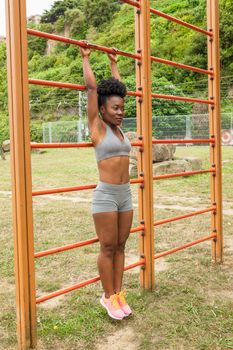 African young woman doing stretching exercises in urban structures for sports in a city park