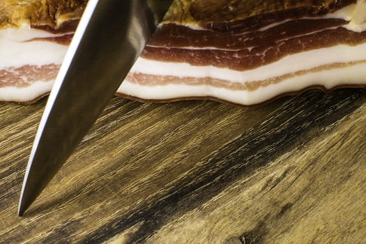 Smoked bacon on vintage wooden board with a knife ready to cut