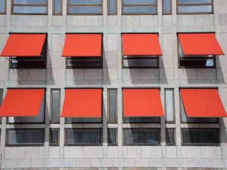 Red Overhang Sunshade Awning with shadows on Grey Building Facade Protecting from the Sun.