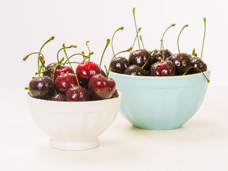 Photo of two bowls of wet cherries over white background.